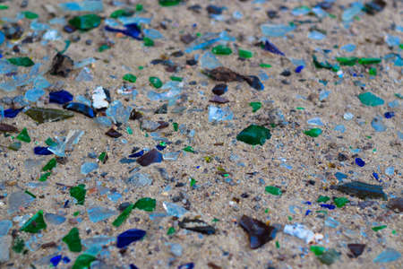 Broken glass bottles on white sand. Bottles is green and blue colour. Trash on the sand. Ecological...