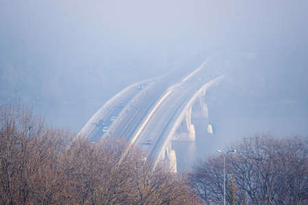 Autumn fog and river steel bridge with subway train on blurred background. Forest in foreground.