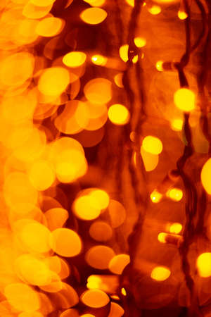 Vertical Christmas garland wall on glass window. Light is orange and defocused. Blurred background,...