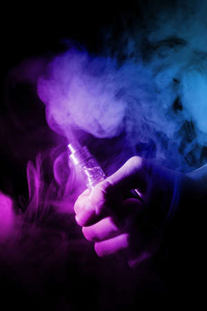 Male hand holds vape in thin vape fog or smoke. Vape clouds around hand with vape on black...