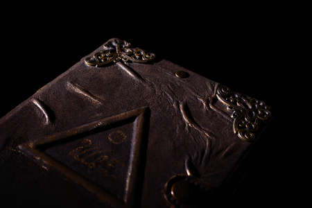 Low light handmade old leather cover notebook. Charred sheets and cover isolated on black background. Underexposed stock photo.の写真素材