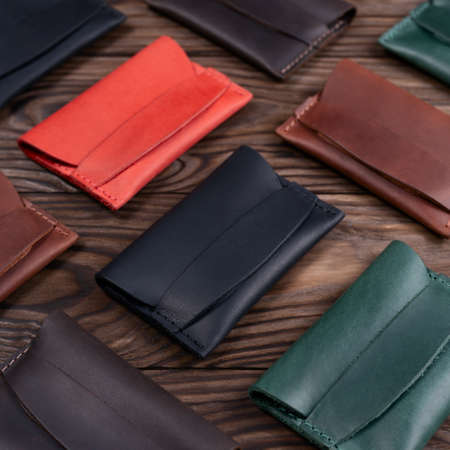 Flat lay photo of five different colour handmade leather one pocket cardholders.  Red, black, blown,...