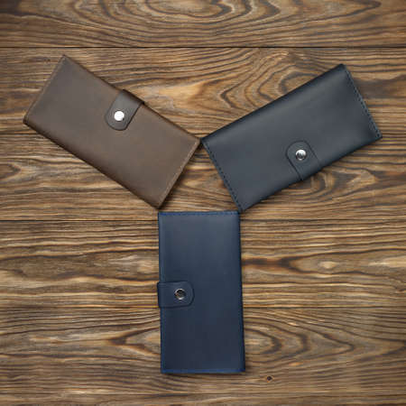 Three handmade leather wallets on textured wooden background. Wallet is unisex. Up to down view....