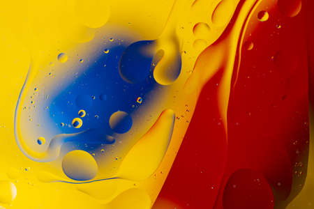 Abstract oil spots in motion on water on blurred yellow background. Red and blue spots on blurred background. Photo with small depth of field.の写真素材
