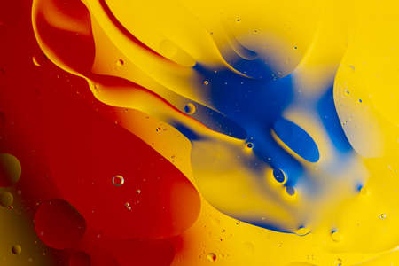 Abstract oil spots in motion on water on blurred yellow background. Red and blue spots on blurred background. Photo with small depth of field.の写真素材