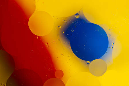 Abstract oil spots in motion on water on blurred yellow background. Red and blue spots on blurred background. Photo with small depth of field.の写真素材