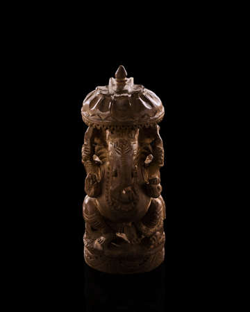 A low light photo of indian god Ganesh statuette. Figurine made of sandalwood. Background is black, statuette is isolated on black bakground. Indian culture figurine photo.の写真素材