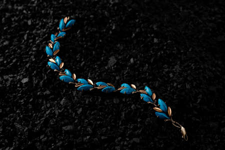 Unique handmade golden bracelet with turquoise inserts on a bunch of small black stones. Creative photo of unique jewellery.の写真素材