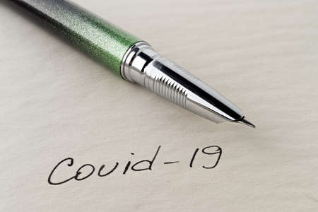Covid-19 inscription on a blank empty sheet of paper in a notebook. Nearby lies a fountain pen. A lot of space for inscriptions and copyspace. The virus is dangerous. Blank for inscriptions. Template for article or cover.の写真素材