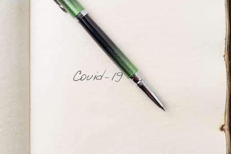 Covid-19 inscription on a blank empty sheet of paper in a notebook. Nearby lies a fountain pen. A...