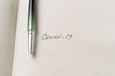 Covid-19 inscription on a blank empty sheet of paper in a notebook. Nearby lies a fountain pen. A lot of space for inscriptions and copyspace. The virus is dangerous. Blank for inscriptions. Template for article or cover.の写真素材