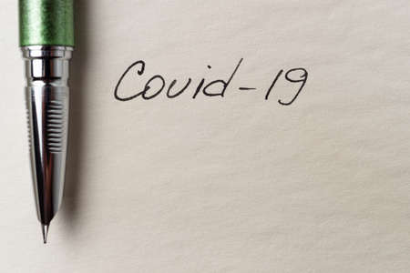 Covid-19 inscription on a blank empty sheet of paper in a notebook. Nearby lies a fountain pen. A...