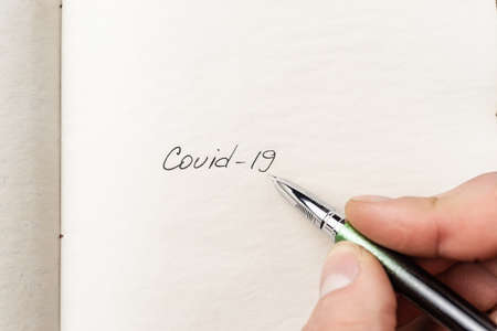 The hand writing Covid-19 on empty sheet of paper. Covid-19 inscription on a blank empty sheet of...
