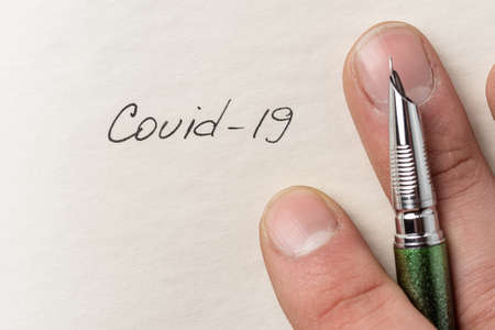 The hand writing Covid-19 on empty sheet of paper. Covid-19 inscription on a blank empty sheet of...
