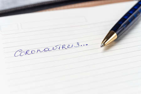 Coronavirus Covid-19 text hand-written on empty sheet in a daily planner. A part of planner on photo. Nearby lies luxury  dark blue ball pen. Sheet with copyspace. Top view.の写真素材