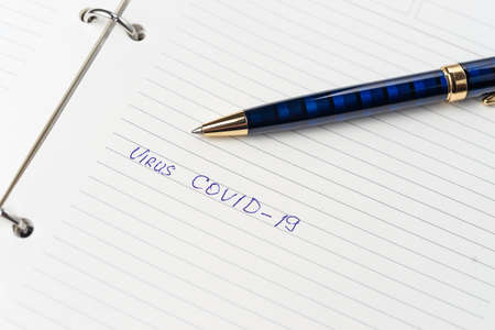 Coronavirus Covid-19 text hand-written on empty sheet in a daily planner. Nearby lies luxury  dark...