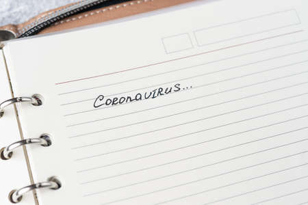 Coronavirus Covid-19 text hand-written on empty sheet in a daily planner. A part of planner on...