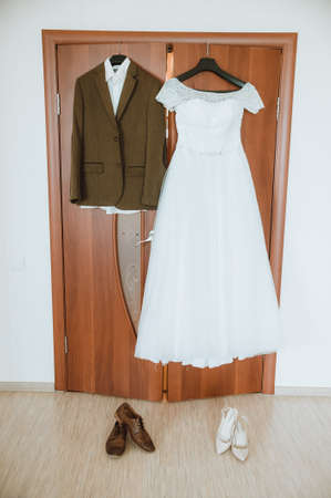 bride dress and groom's suit on a hanger, hanging in the room on the doorの写真素材