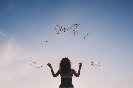 A young woman throws yellow flowers in the air against the blue sky. dandelionsの写真素材