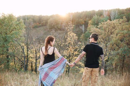 man in a black T-shirt and a pregnant woman in a black dress and dreadlocks embrace and are kept in hand, against the background of wild nature, autumn. love storyの写真素材
