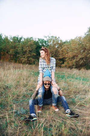 young guy in a cap and solar oskah, with a beard and mustache, and tattooed, with his pregnant girl in dreadlocks, outdoors in the fall posing at the camera,の写真素材