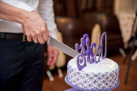 Happy wedding couple handsome groom and blonde bride carving delicious wedding cakeの写真素材