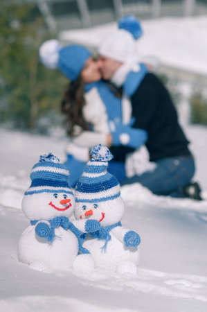 handmade knitted snowman in the snow, on a background of the kissing coupleの写真素材