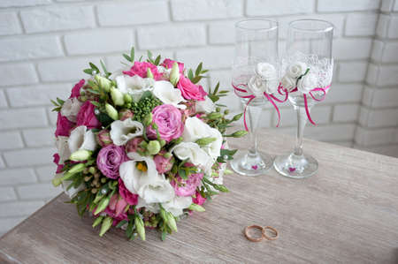 bridal bouquet with wedding rings and wedding wine glasses on the table in the morning of the wedding dayの写真素材