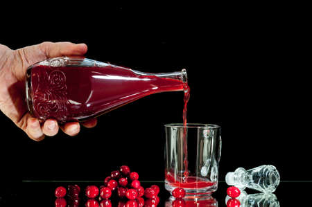 hand man pours red liqueur, cranberry juice,  , isolated on a black background.の写真素材