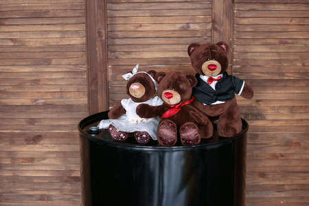 Soft toys, a family of bears, on a barrel of motor oil, against a wooden wallの写真素材