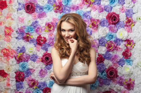 Beautiful woman smiling, wearing a wedding dress on a background of flowers. Emotion shynessの写真素材