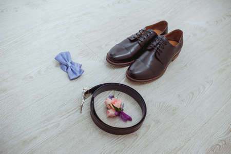 Boutonniere of the groom of a rose, a blue bow tie, brown shoes and a belt for the groomの写真素材