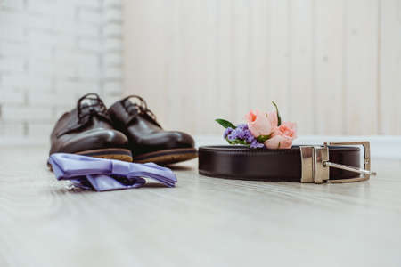 Boutonniere of the groom of a rose, a blue bow tie, brown shoes and a belt for the groomの写真素材