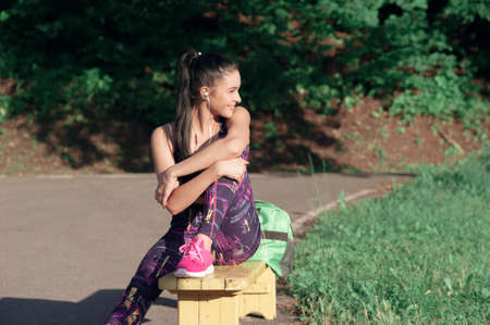 Concept of sport and lifestyle - young woman having a rest after playing sports smiling sitting on a bench, outdoorsの写真素材