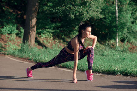 Concept of sport and lifestyle - young woman doing warm-up, smiling, outdoorsの写真素材
