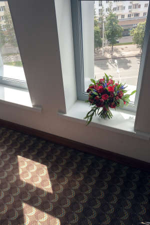 Bride bouquet of red roses before the wedding, stands on the window overlooking the street of the cityの写真素材