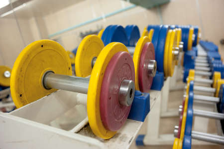 Dumbbells with yellow and red cargo disks in the gym lie in a row. backgroundの写真素材