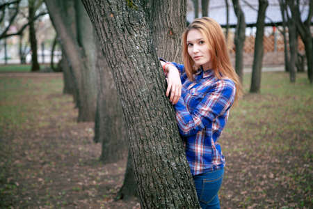 Portrait of a beautiful girl. smiling, posing on camera. in a blue shirt in a cage. Against the background of the autumn parkの写真素材
