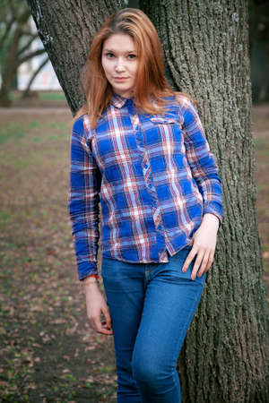 Portrait of a beautiful girl. smiling, posing on camera. in a blue shirt in a cage. Against the background of the autumn parkの写真素材