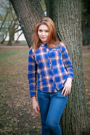 Portrait of a beautiful girl. smiling, posing on camera. in a blue shirt in a cage. Against the background of the autumn parkの写真素材