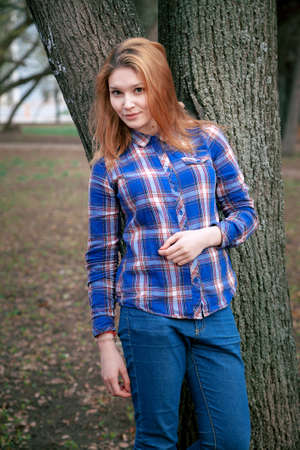 Portrait of a beautiful girl. smiling, posing on camera. in a blue shirt in a cage. Against the background of the autumn parkの写真素材