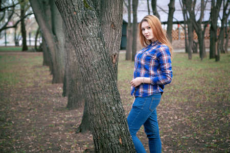 Portrait of a beautiful girl. smiling, posing on camera. in a blue shirt in a cage. Against the background of the autumn parkの写真素材