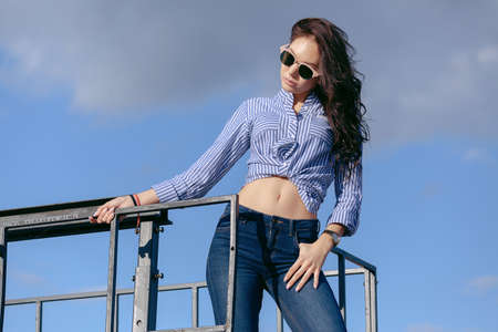 A beautiful girl with sunglasses and torn jeans and a striped shirt. Against the background of large...