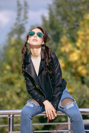 fashionable young woman in rock style clothes, black leather jacket, blue jeans, tights in a grid under battered jeansの写真素材