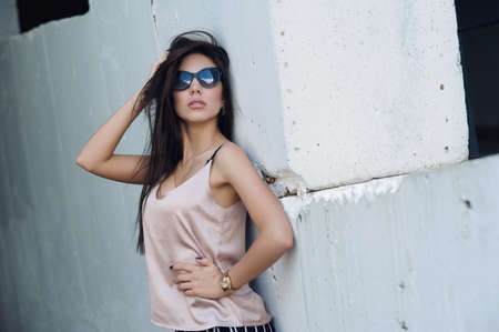 A beautiful girl with sunglasses in a beige T-shirt. Against the background of large concrete structures. Artistic photography. beauty and fashion, styleの写真素材