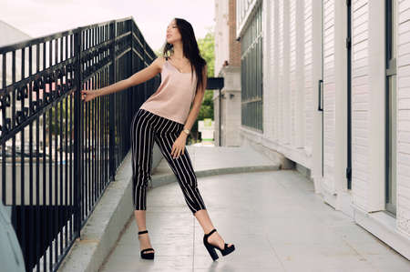 Beautiful young woman standing at the entrance to the underground garage. The model wears stylish clothes, a beige jersey, and black breeches in a white stripe. The girl is looking up, the hair is developing in the wind. Women's fashion. Urban way of lifeの写真素材