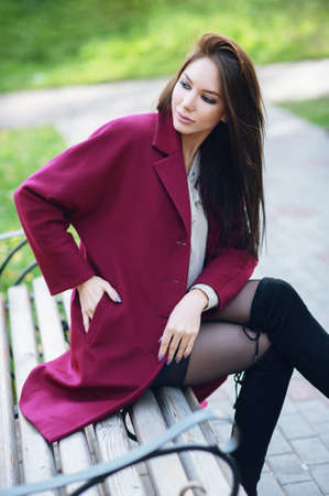 Young beautiful stylish woman walking in burgundy coat, street style, spring summer trend, dark skirt, beige jacket, flirty.の写真素材