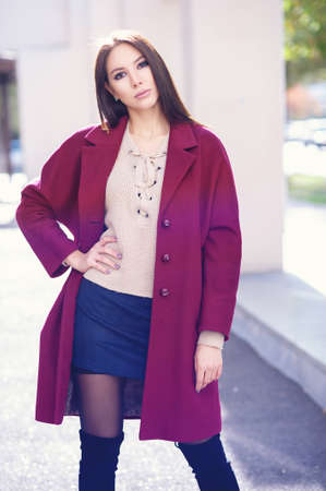 Young beautiful stylish woman walking in burgundy coat, street style, spring summer trend, dark skirt, beige jacket, flirty.の写真素材