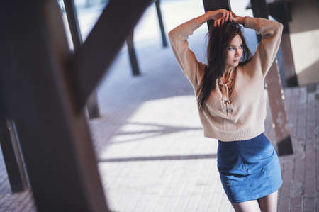 Portrait of a charming young woman in a knitted woolen beige sweater, on a wooden stall background. Hides half of face, and poses on camera.の写真素材