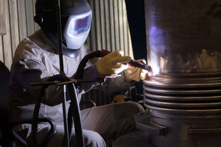 Welder with protective mask welding metal and sparks.